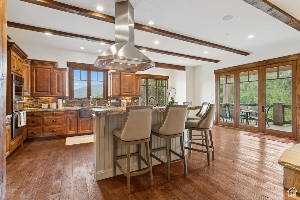 Kitchen featuring island range hood, oven, brown cabinetry, beam ceiling, and recessed lighting