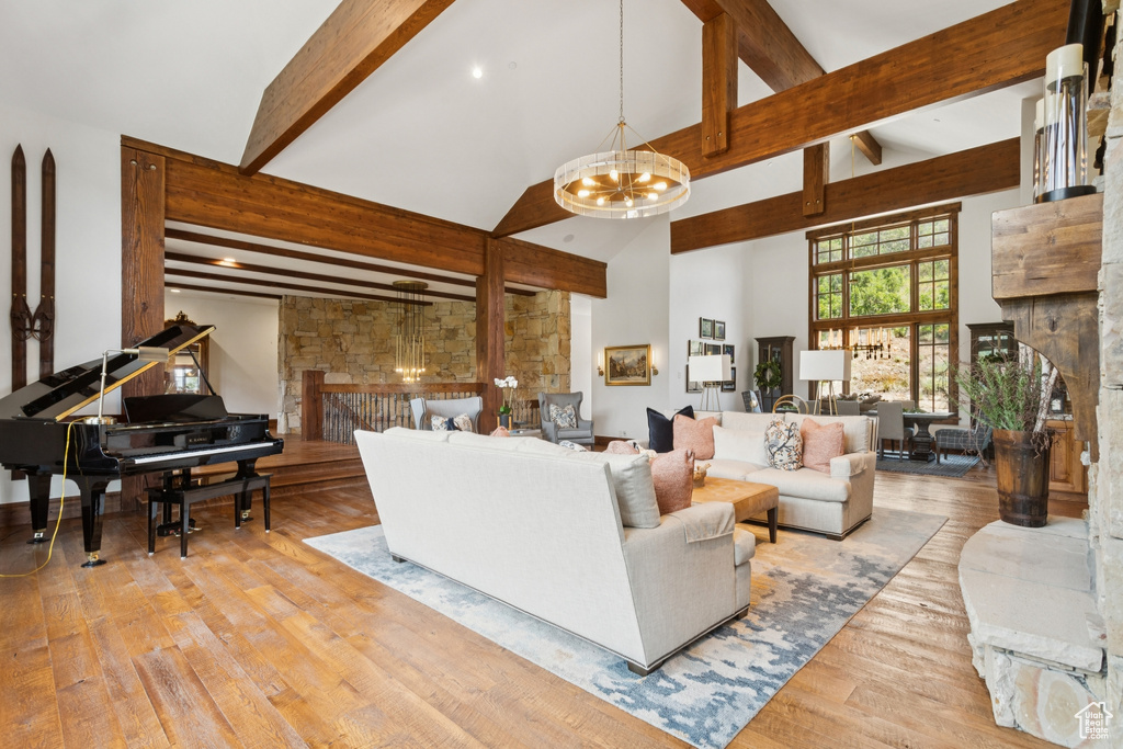 Living room with a fireplace, beamed ceiling, a chandelier, wood finished floors, and high vaulted ceiling