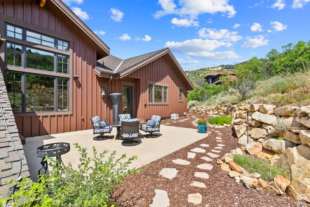 Rear view of property featuring a patio, a shingled roof, board and batten siding, and an outdoor fire pit