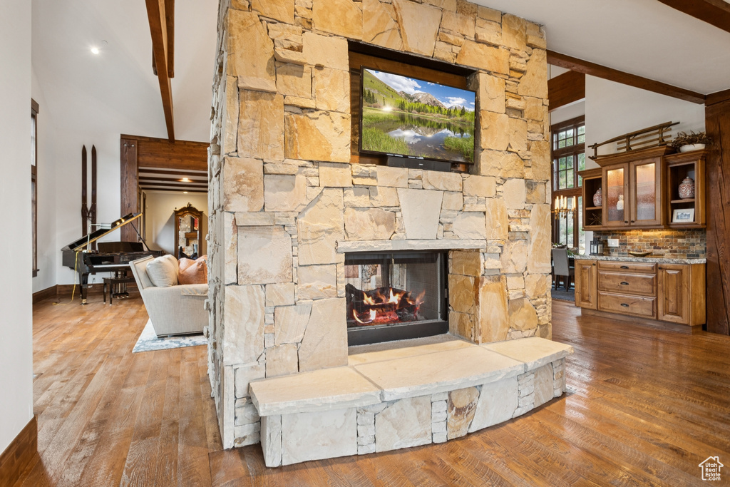 Unfurnished living room with beam ceiling, wood finished floors, high vaulted ceiling, and a stone fireplace
