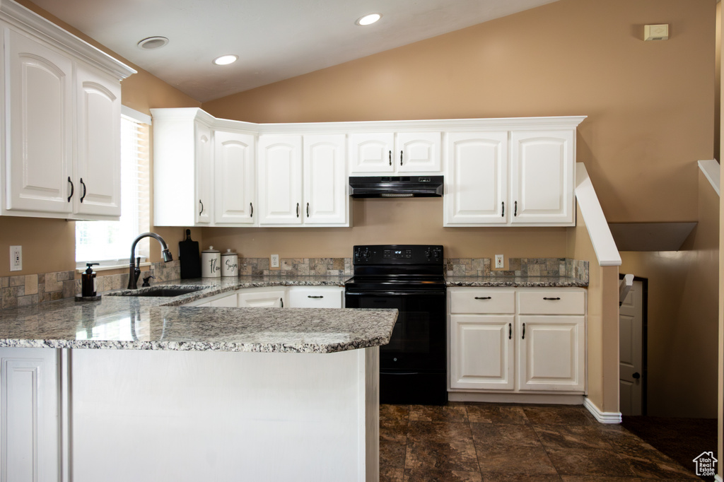 Kitchen featuring black range with electric stovetop, under cabinet range hood, vaulted ceiling, a peninsula, and light stone counters