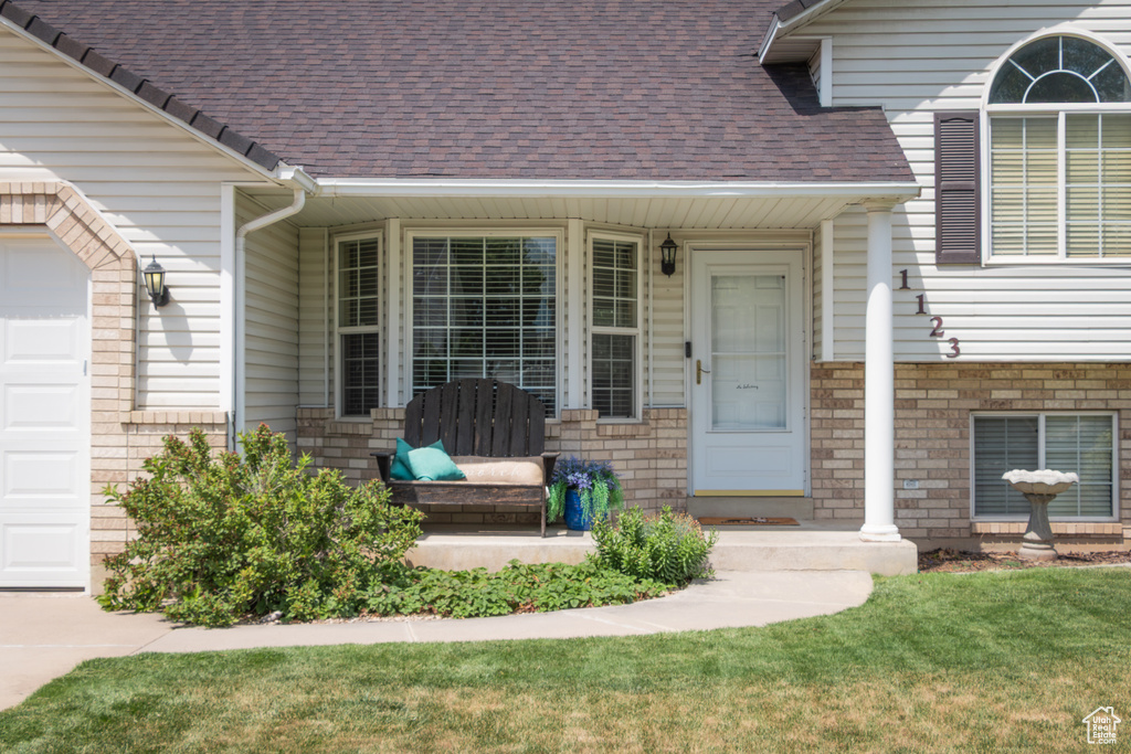 Entrance to property with an attached garage, roof with shingles, and brick siding