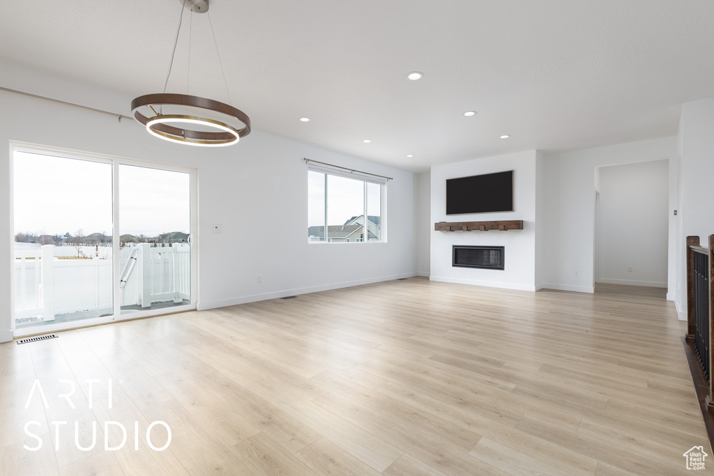 Unfurnished living room featuring a glass covered fireplace, light wood finished floors, a chandelier, and recessed lighting