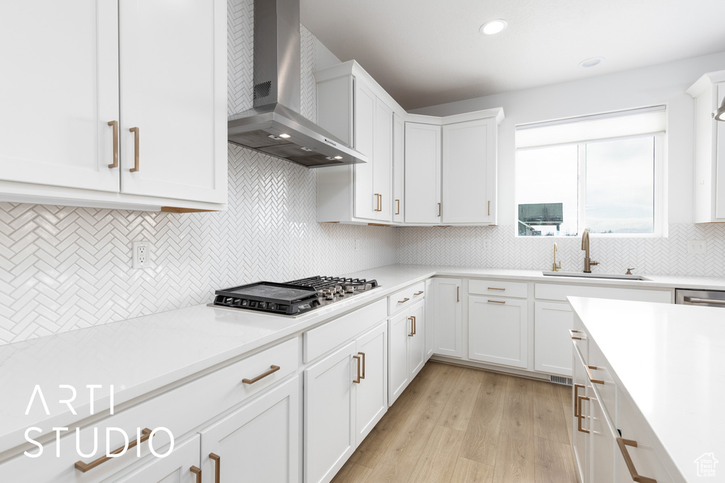 Kitchen featuring wall chimney exhaust hood, stainless steel gas cooktop, light wood finished floors, light countertops, and white cabinetry