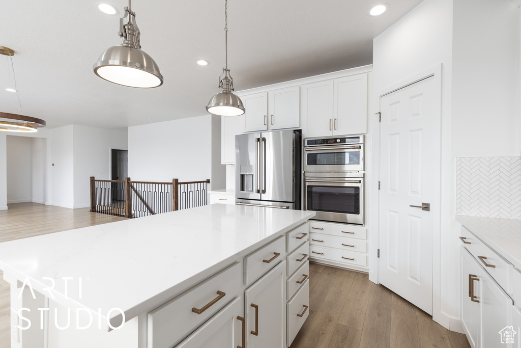 Kitchen with appliances with stainless steel finishes, hanging light fixtures, light wood-type flooring, backsplash, and light countertops