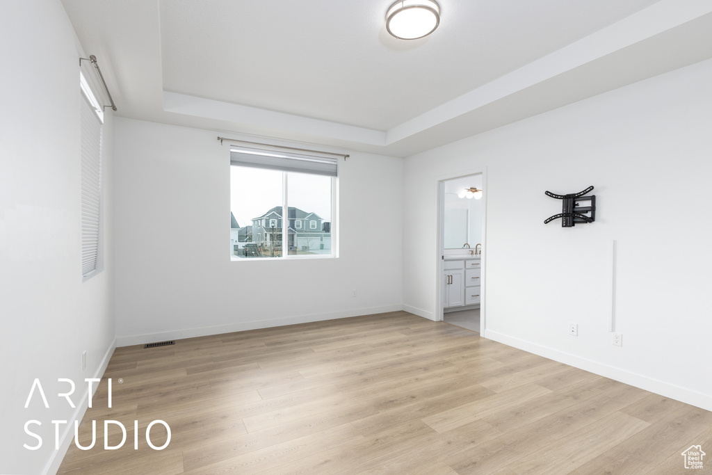 Spare room with a tray ceiling and light wood-style floors