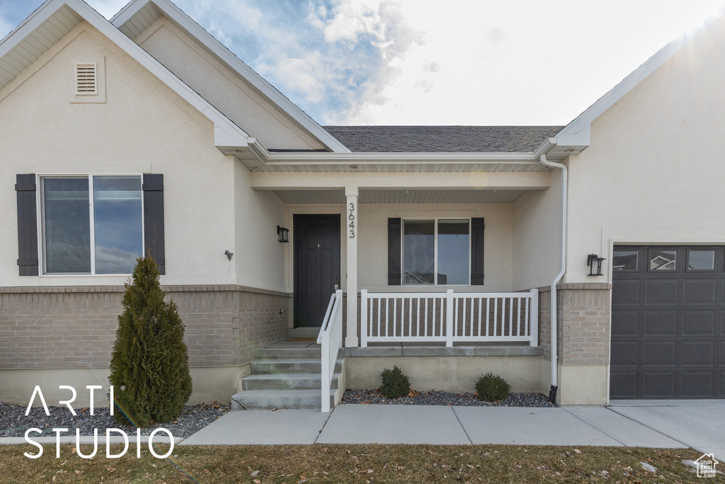 View of front of property with covered porch, stucco siding, brick siding, and an attached garage