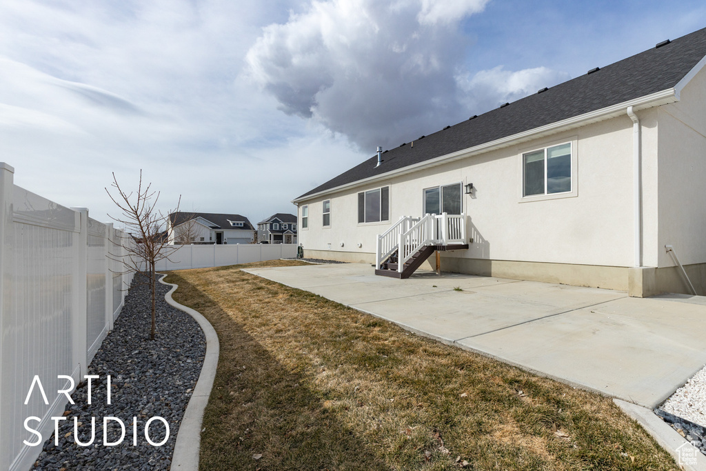 Rear view of house with a fenced backyard, a patio, roof with shingles, and stucco siding