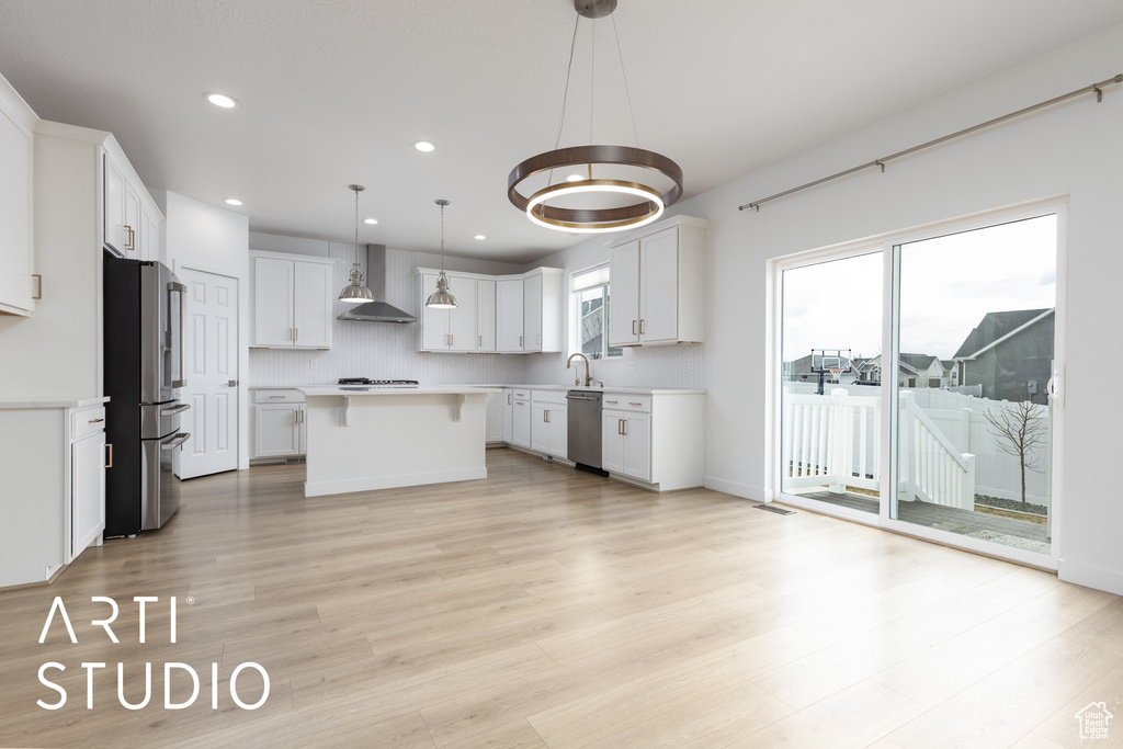Kitchen with wall chimney exhaust hood, appliances with stainless steel finishes, a kitchen island, light countertops, and recessed lighting