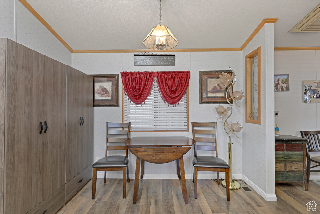 Dining area with wood finished floors, crown molding, and wallpapered walls