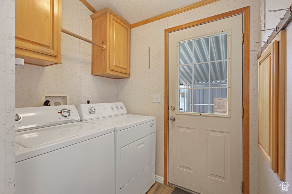 Laundry room with cabinet space, washing machine and dryer, wallpapered walls, and ornamental molding
