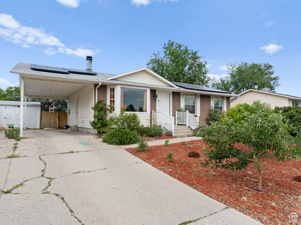 View of front of property with driveway, roof mounted solar panels, a carport, a gate, and brick siding