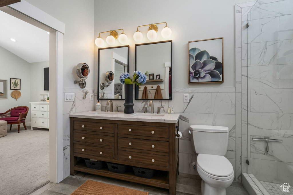 Full bathroom featuring vanity, a stall shower, tile walls, vaulted ceiling, and wainscoting