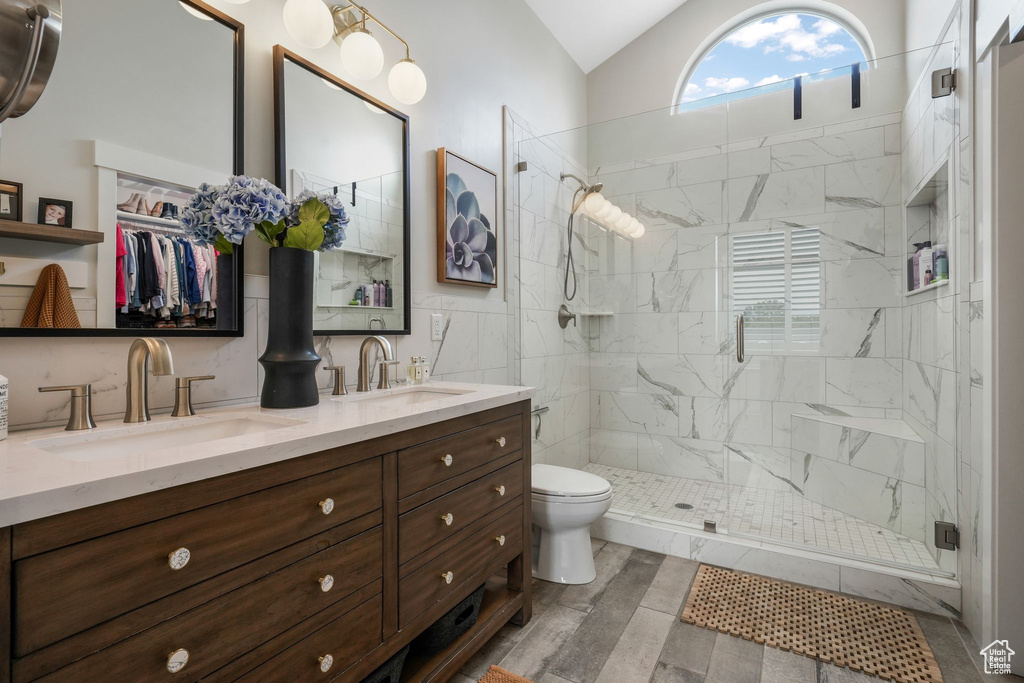 Bathroom with double vanity, a shower stall, lofted ceiling, and wood finished floors
