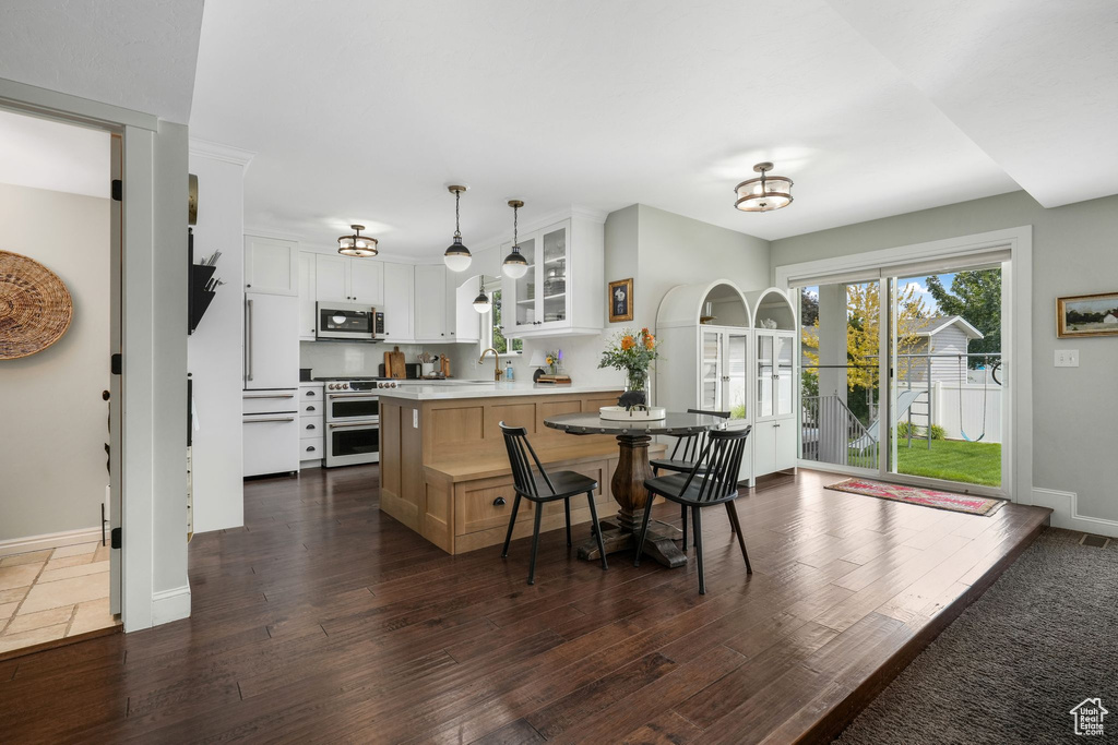 Kitchen with appliances with stainless steel finishes, glass insert cabinets, a peninsula, light countertops, and dark wood-style floors