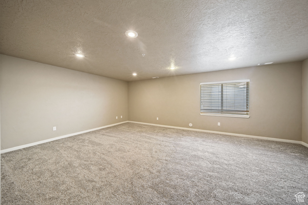 Carpeted empty room with a textured ceiling and recessed lighting