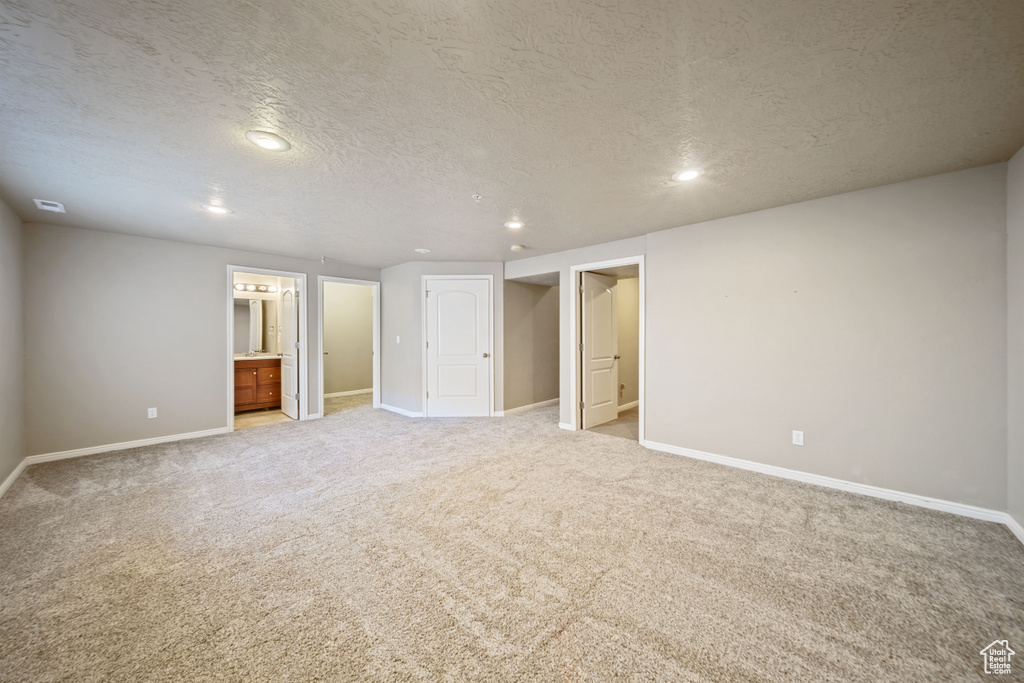 Unfurnished bedroom with light carpet, recessed lighting, a textured ceiling, and connected bathroom