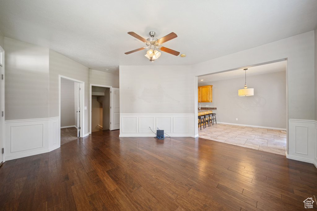 Unfurnished living room with a ceiling fan, wainscoting, wood finished floors, and a decorative wall