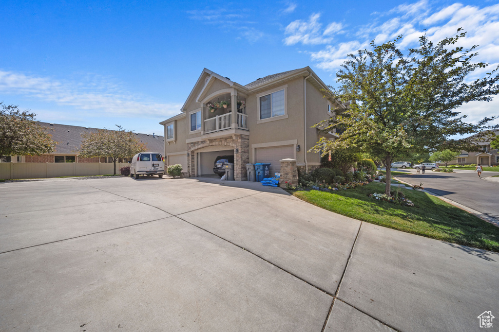View of front of house featuring an attached garage, stone siding, concrete driveway, stucco siding, and a balcony