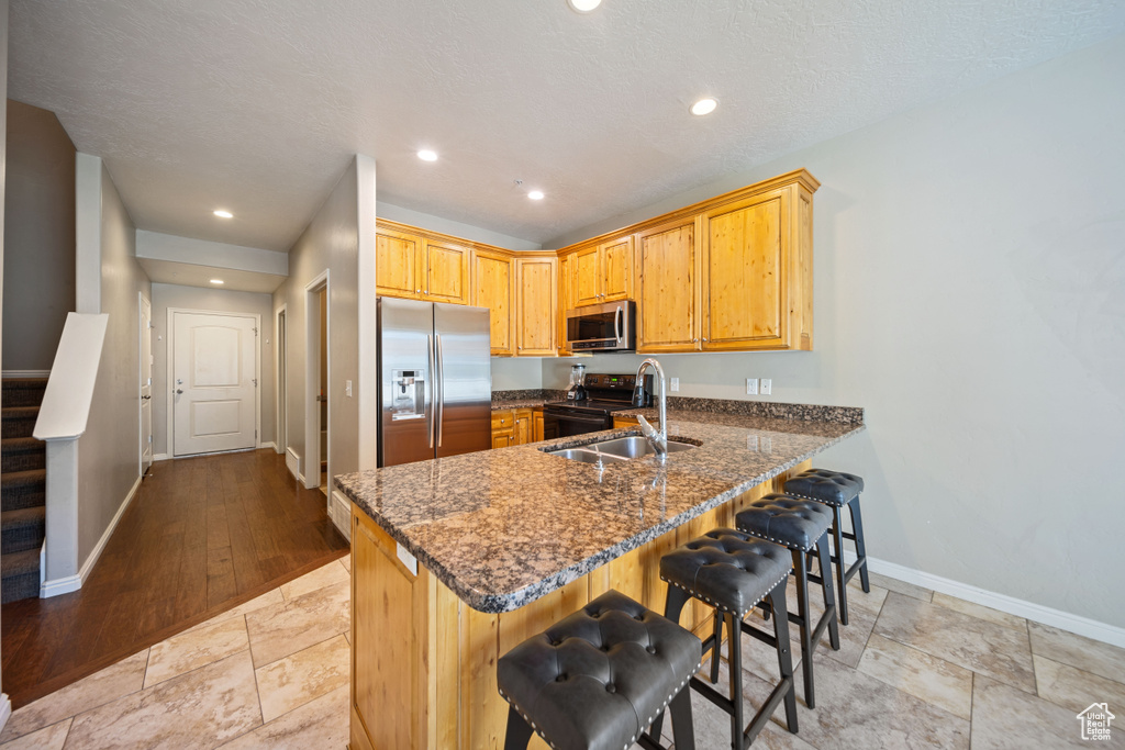Kitchen with appliances with stainless steel finishes, a peninsula, dark stone countertops, a kitchen breakfast bar, and recessed lighting