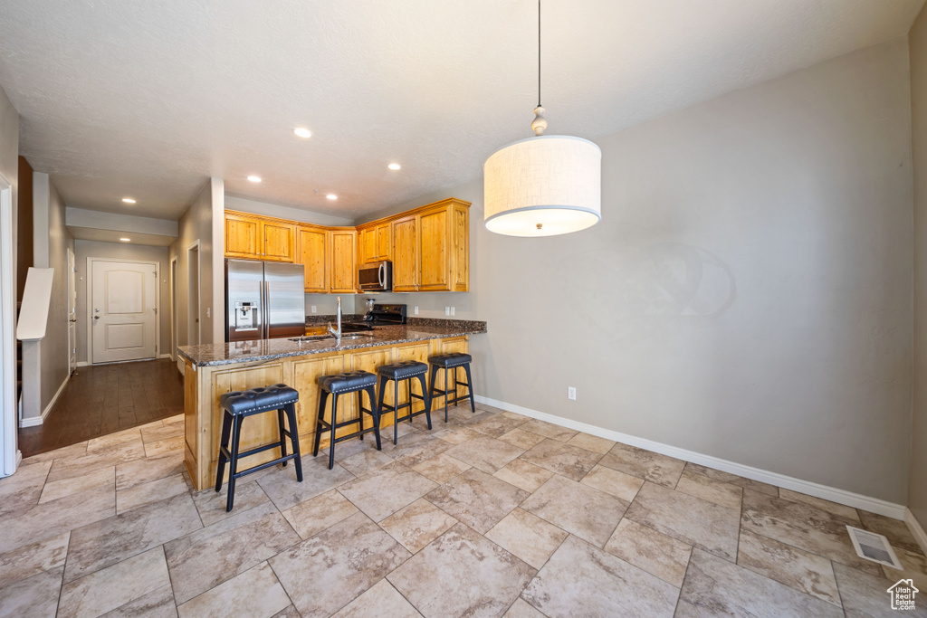 Kitchen featuring stainless steel appliances, stone tile flooring, dark stone counters, a peninsula, and recessed lighting