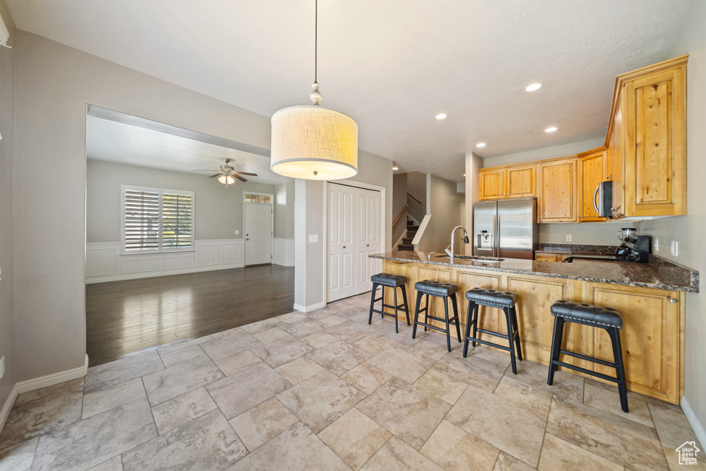 Kitchen featuring appliances with stainless steel finishes, a ceiling fan, stone tile flooring, a peninsula, and dark stone countertops