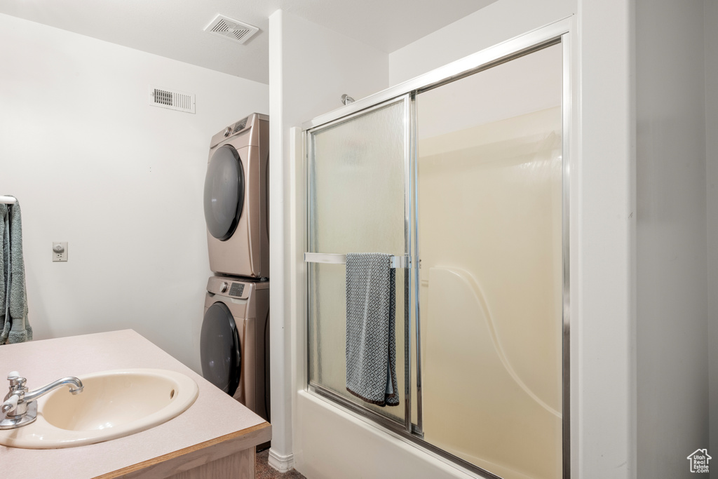 Bathroom with stacked washing machine and dryer, vanity, and bath / shower combo with glass door