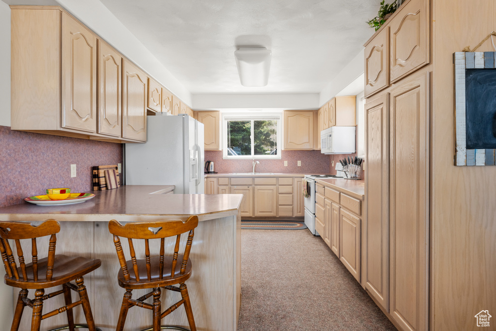 Kitchen with white appliances, light brown cabinets, a peninsula, a kitchen breakfast bar, and tasteful backsplash