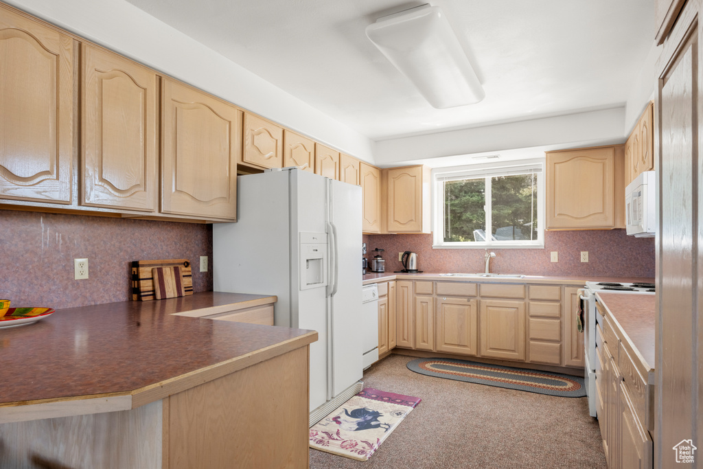 Kitchen with white appliances, light brown cabinetry, tasteful backsplash, and a peninsula