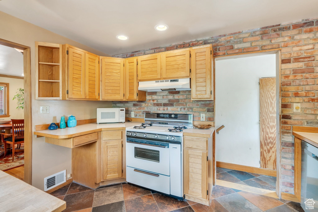 Kitchen featuring white appliances, under cabinet range hood, light countertops, dark stone finish floors, and open shelves