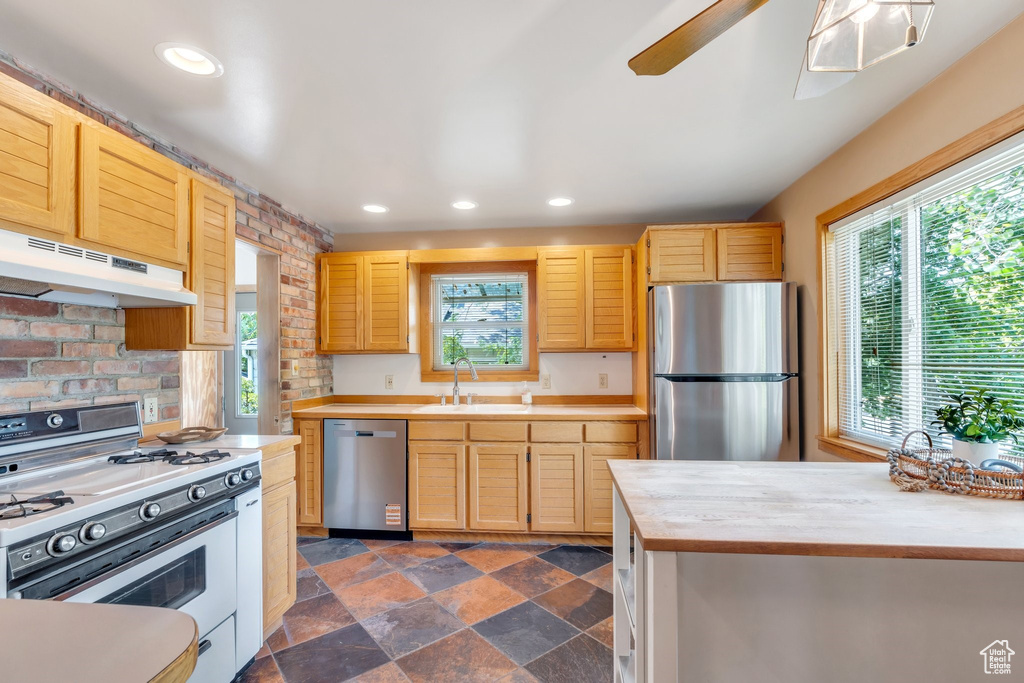 Kitchen with stainless steel appliances, under cabinet range hood, light countertops, dark stone finish flooring, and a ceiling fan