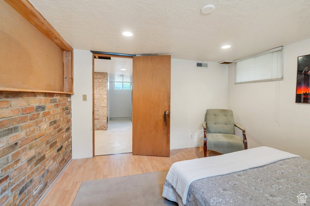 Bedroom with wood finished floors, brick wall, and recessed lighting