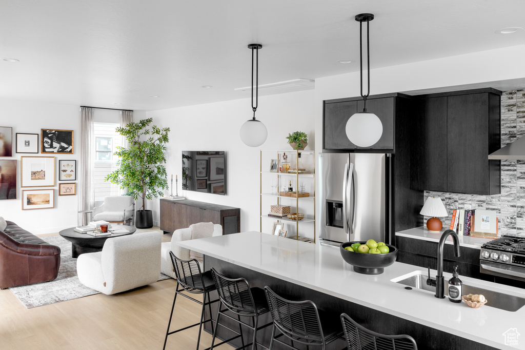 Kitchen with appliances with stainless steel finishes, dark cabinetry, open floor plan, a breakfast bar area, and light countertops