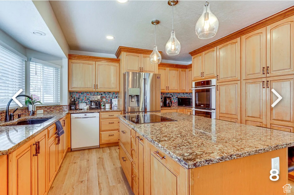 Kitchen featuring stainless steel appliances, light brown cabinetry, a center island, light stone countertops, and light wood-style floors