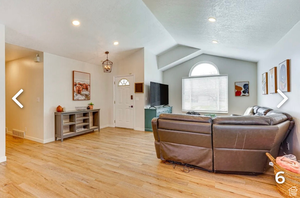 Living area featuring vaulted ceiling, light wood-style floors, and a chandelier