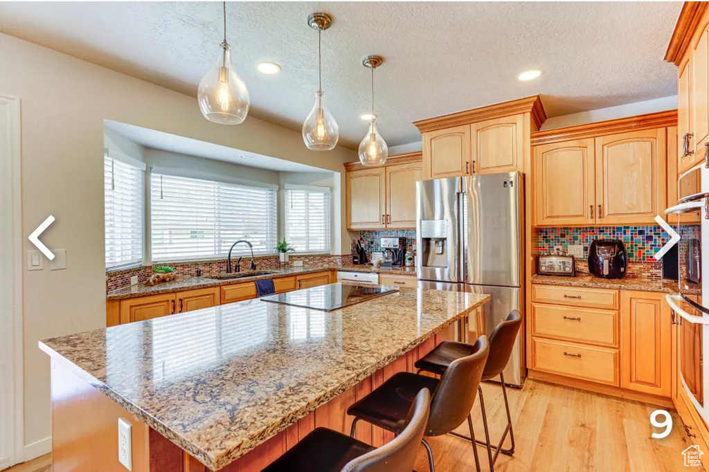 Kitchen with stainless steel refrigerator with ice dispenser, light wood-type flooring, a kitchen island, backsplash, and a breakfast bar area