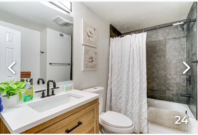 Full bathroom with vanity, shower / bath combo, and a textured ceiling