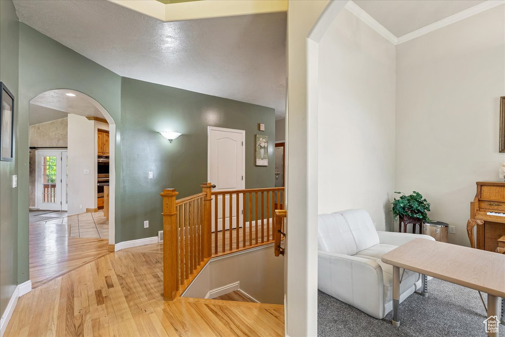 Hallway featuring arched walkways, an upstairs landing, light wood-type flooring, and crown molding