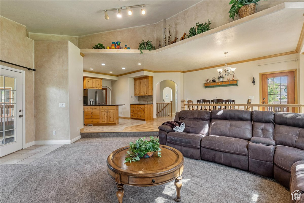 Living area with arched walkways, a chandelier, light tile patterned floors, light carpet, and crown molding