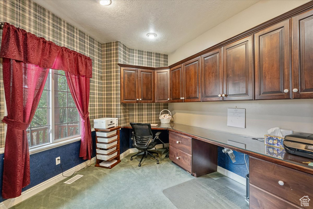 Home office with built in study area, wallpapered walls, a textured ceiling, and carpet floors
