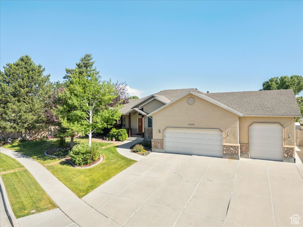 View of front facade with stucco siding, a garage, concrete driveway, a front lawn, and stone siding