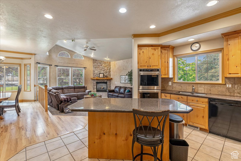 Kitchen featuring black dishwasher, stainless steel double oven, a center island, a breakfast bar area, and light tile patterned floors
