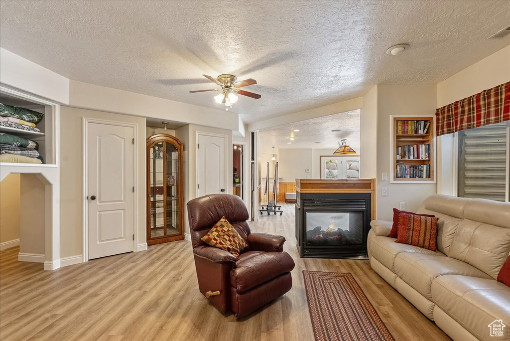 Living area with a textured ceiling, light wood-type flooring, a multi sided fireplace, ceiling fan, and built in shelves
