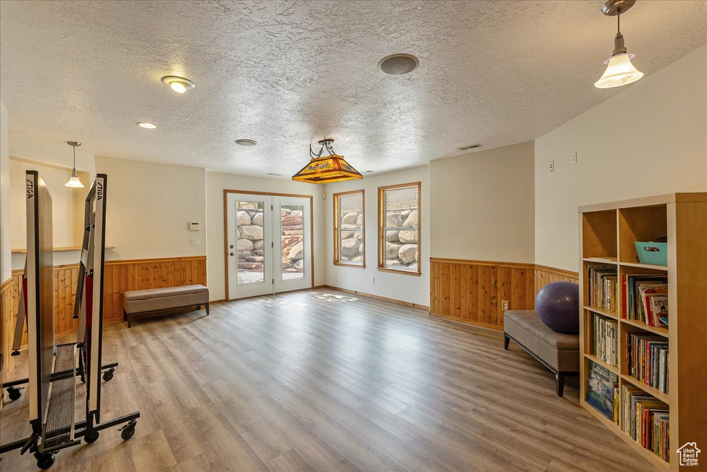 Unfurnished room with a wainscoted wall, wooden walls, a textured ceiling, wood finished floors, and french doors