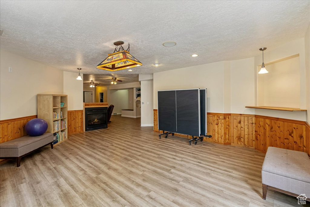 Exercise area featuring a wainscoted wall, a warm lit fireplace, a textured ceiling, wooden walls, and light wood-type flooring