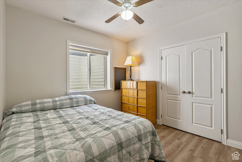 Bedroom with light wood-style flooring, a textured ceiling, a closet, and a ceiling fan