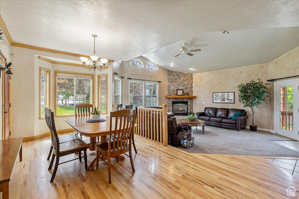 Dining room with a textured ceiling, light wood-style floors, a fireplace, lofted ceiling, and a chandelier