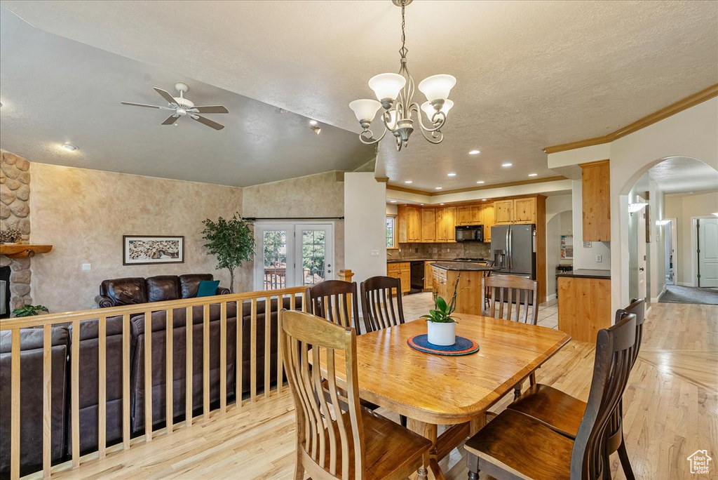 Dining area with light wood-style floors, a ceiling fan, arched walkways, a chandelier, and lofted ceiling