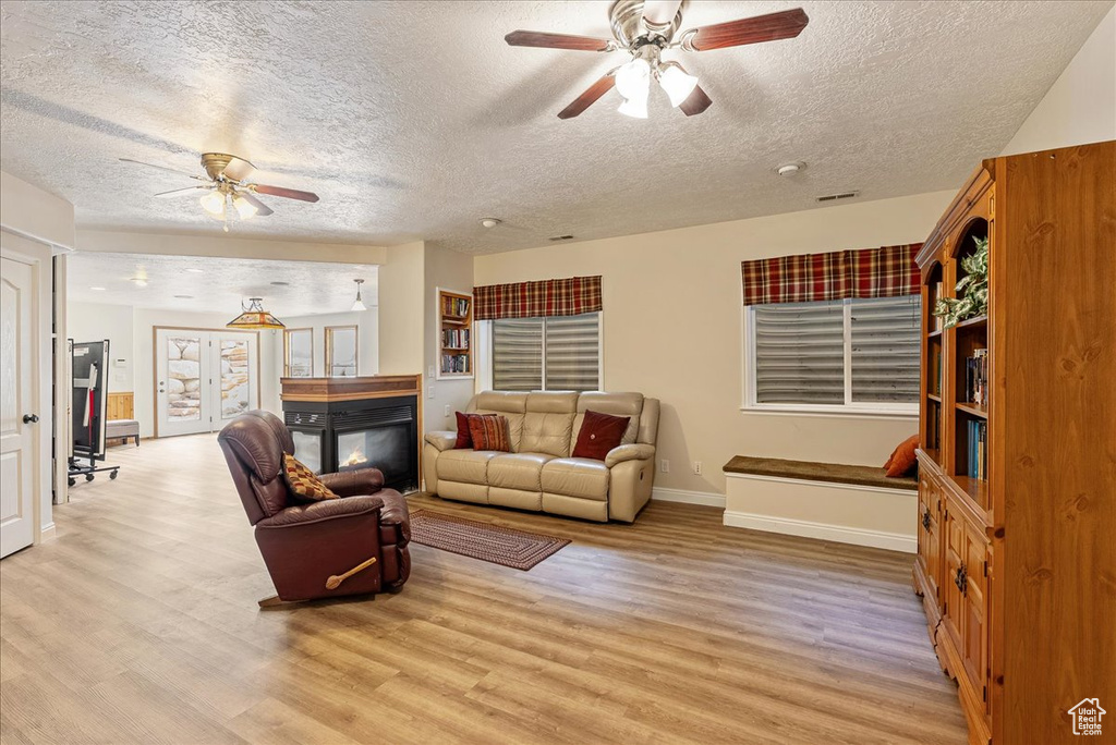 Living area featuring a ceiling fan, a textured ceiling, light wood-style floors, and a multi sided fireplace