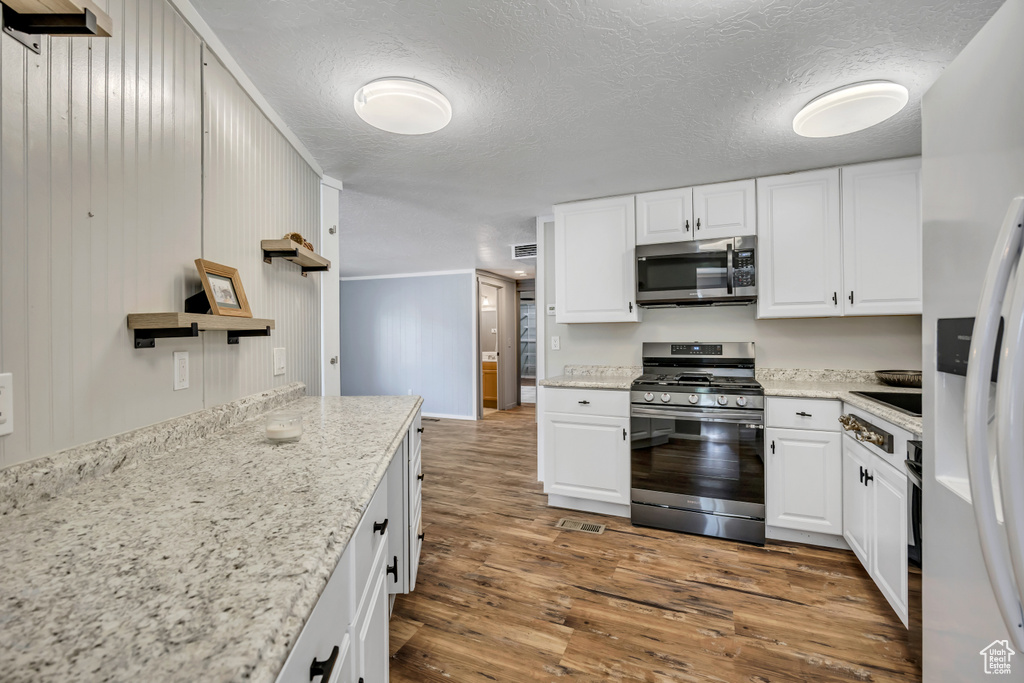 Kitchen with stainless steel appliances, white cabinetry, dark wood-style floors, and a textured ceiling